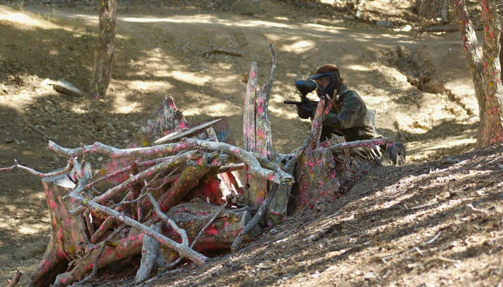 paintball player taking cover behind some tree stumps.