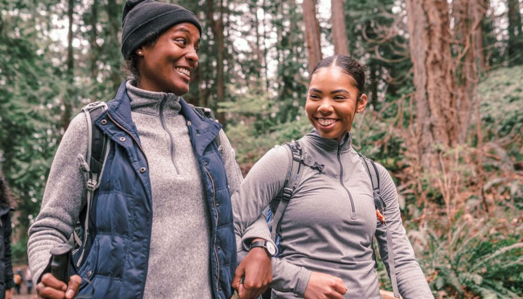 two women hiking in the woods while linking their arms